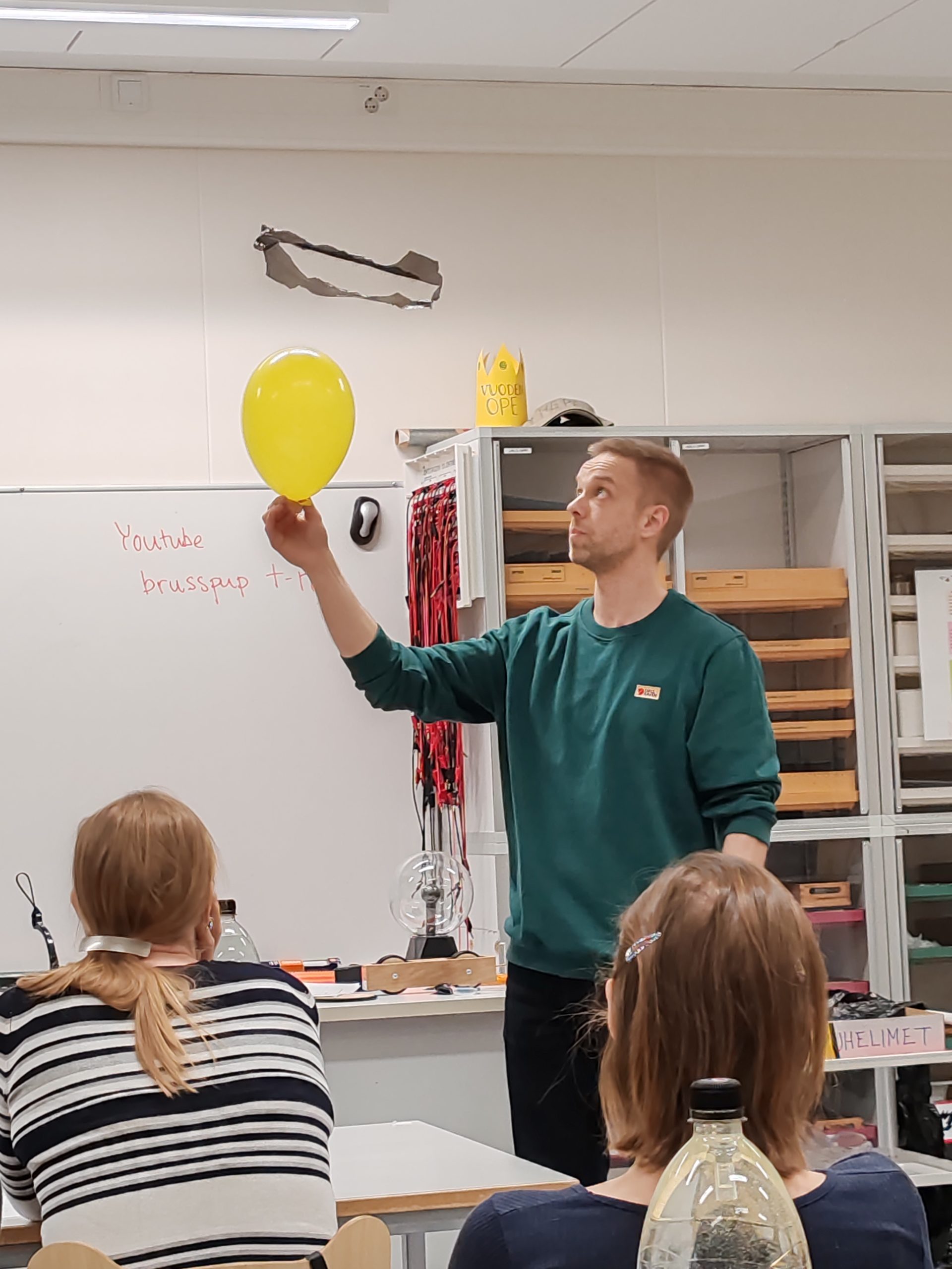 Luokan edessä Jukka seisoo käsissään ilmapallo, jonka yläpuolella leijuu muovipussista leikattu ympyrä.